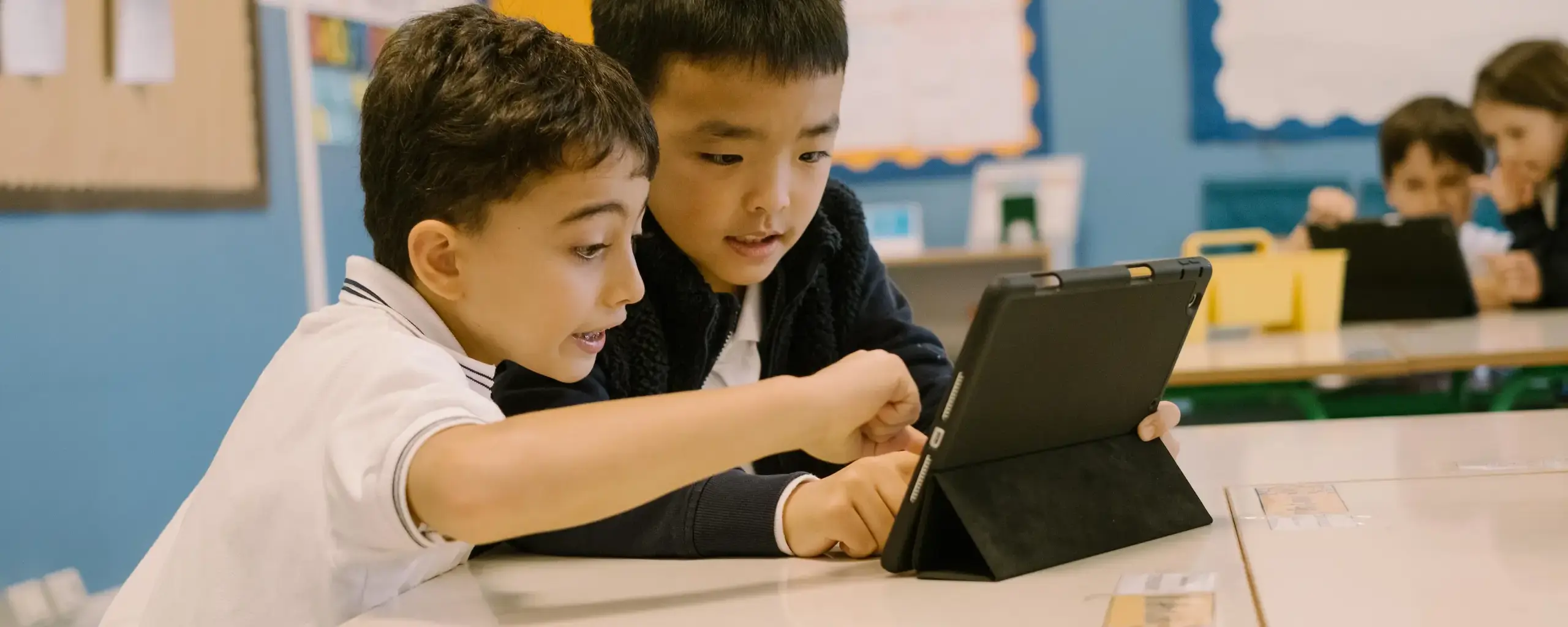 two students working together on a tablet at their classroom desk.