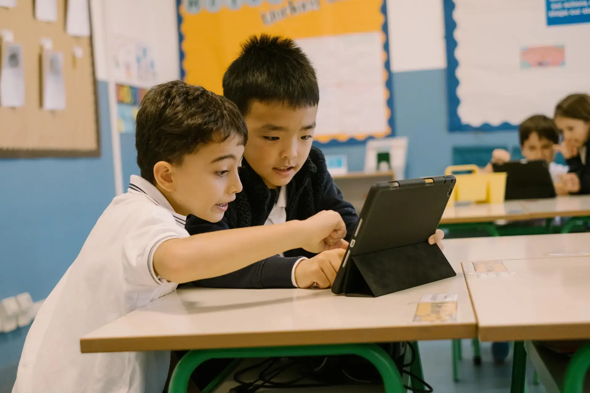 two students working together on a tablet at their classroom desk.