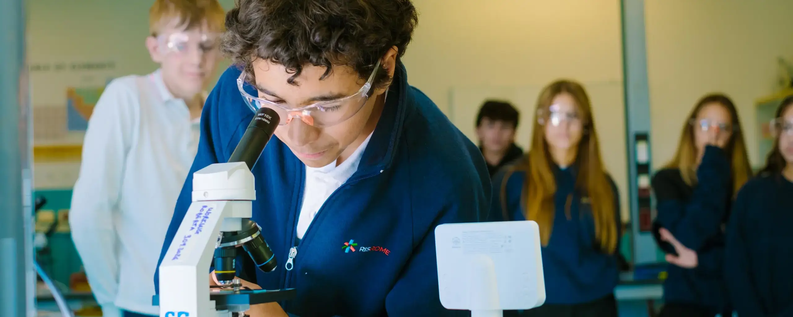 high school student wearing safety goggles looking through a microscope in the science lab.