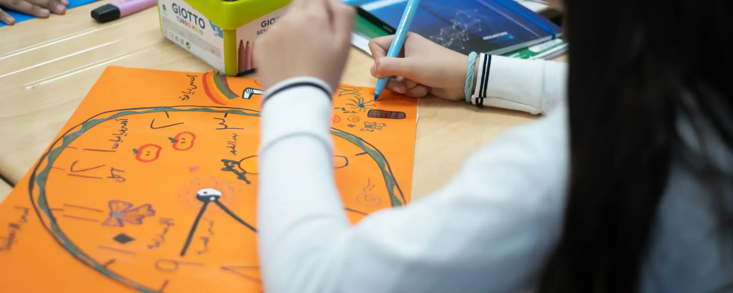 student drawing a colorful project poster with markers at her desk.