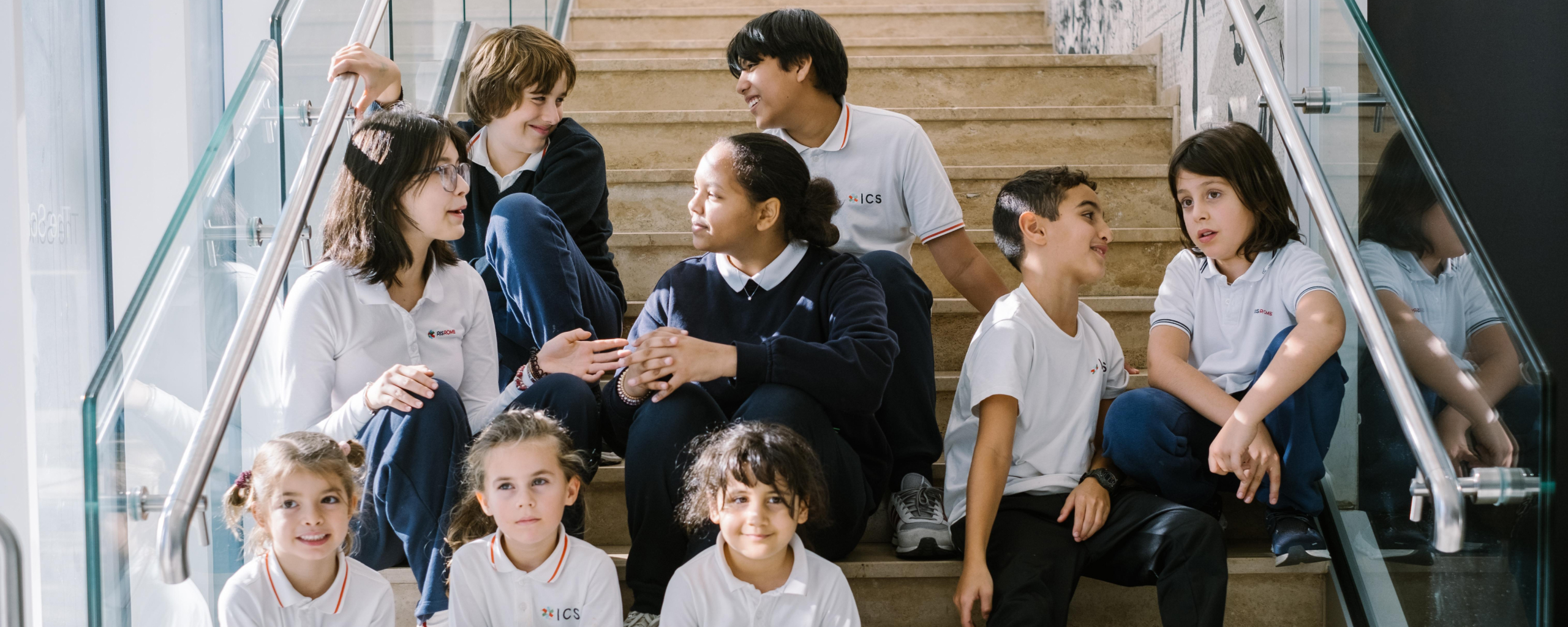 students in school uniforms sitting together on a staircase talking and smiling