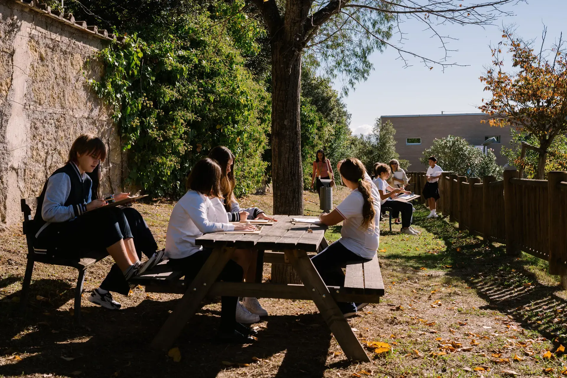 students working at outdoor picnic tables on the school grounds.