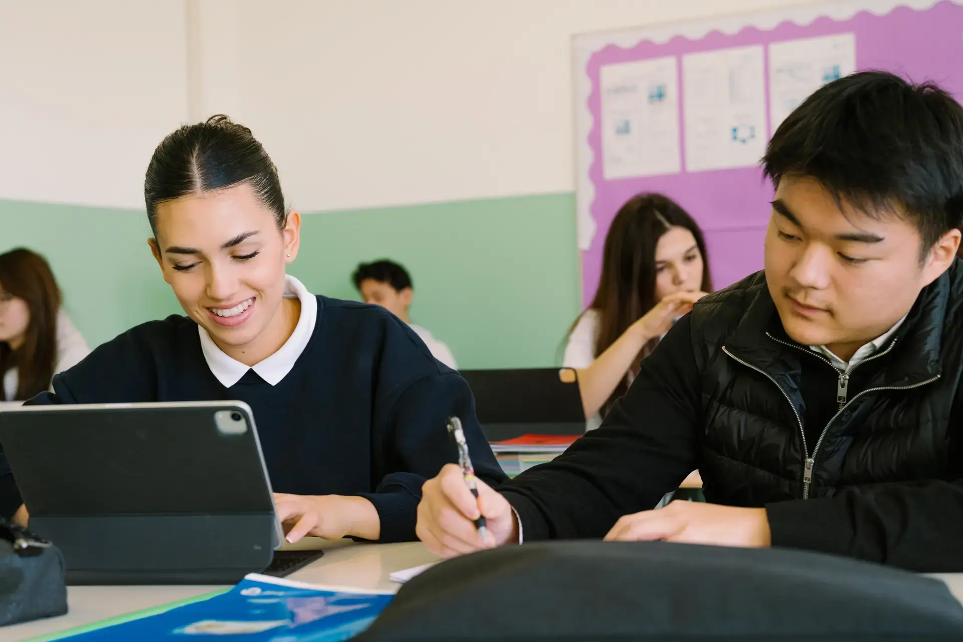 students working together on a tablet and notebook at their desk.