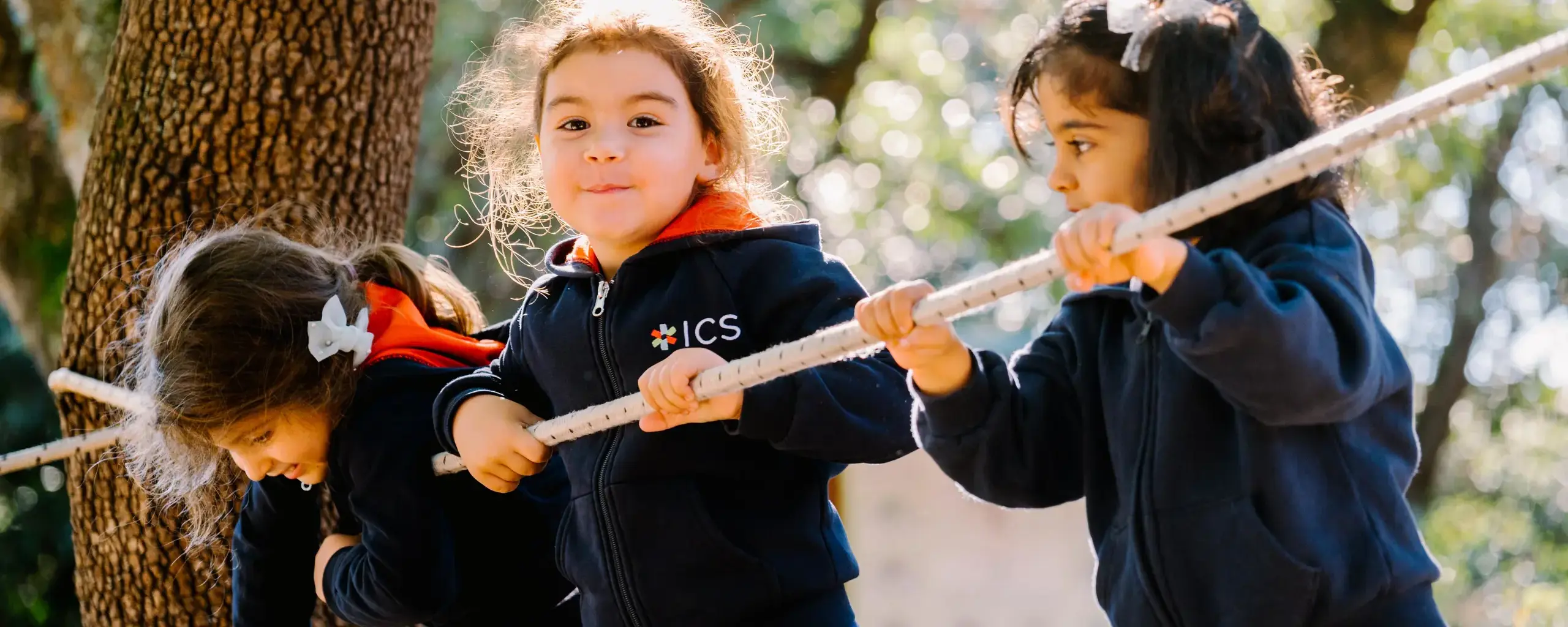 young students holding a measuring stick together outdoors during an activity among the trees.