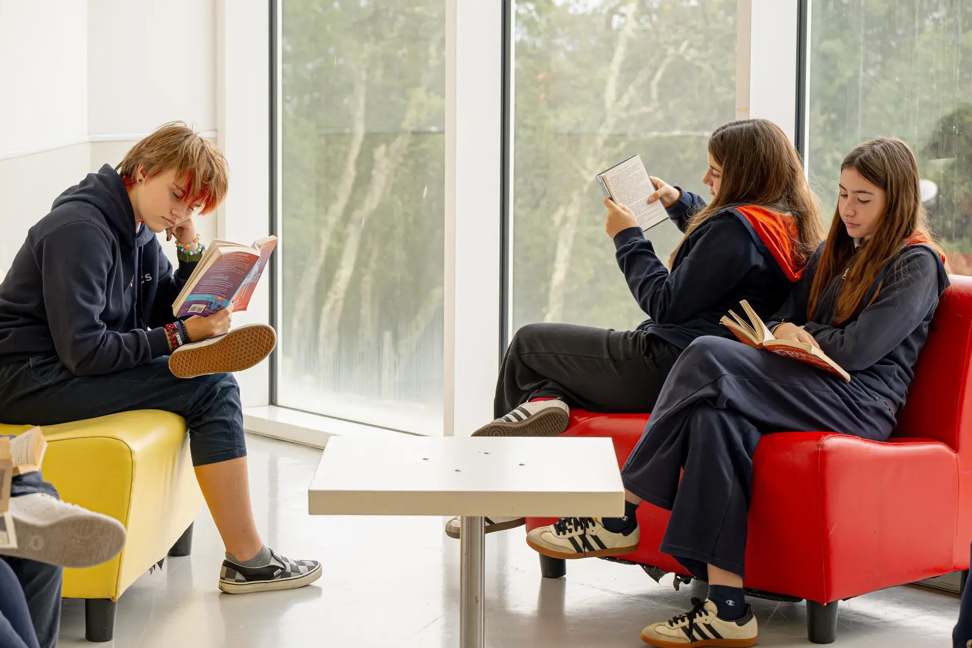 students reading and relaxing together on lounge seating by large windows.