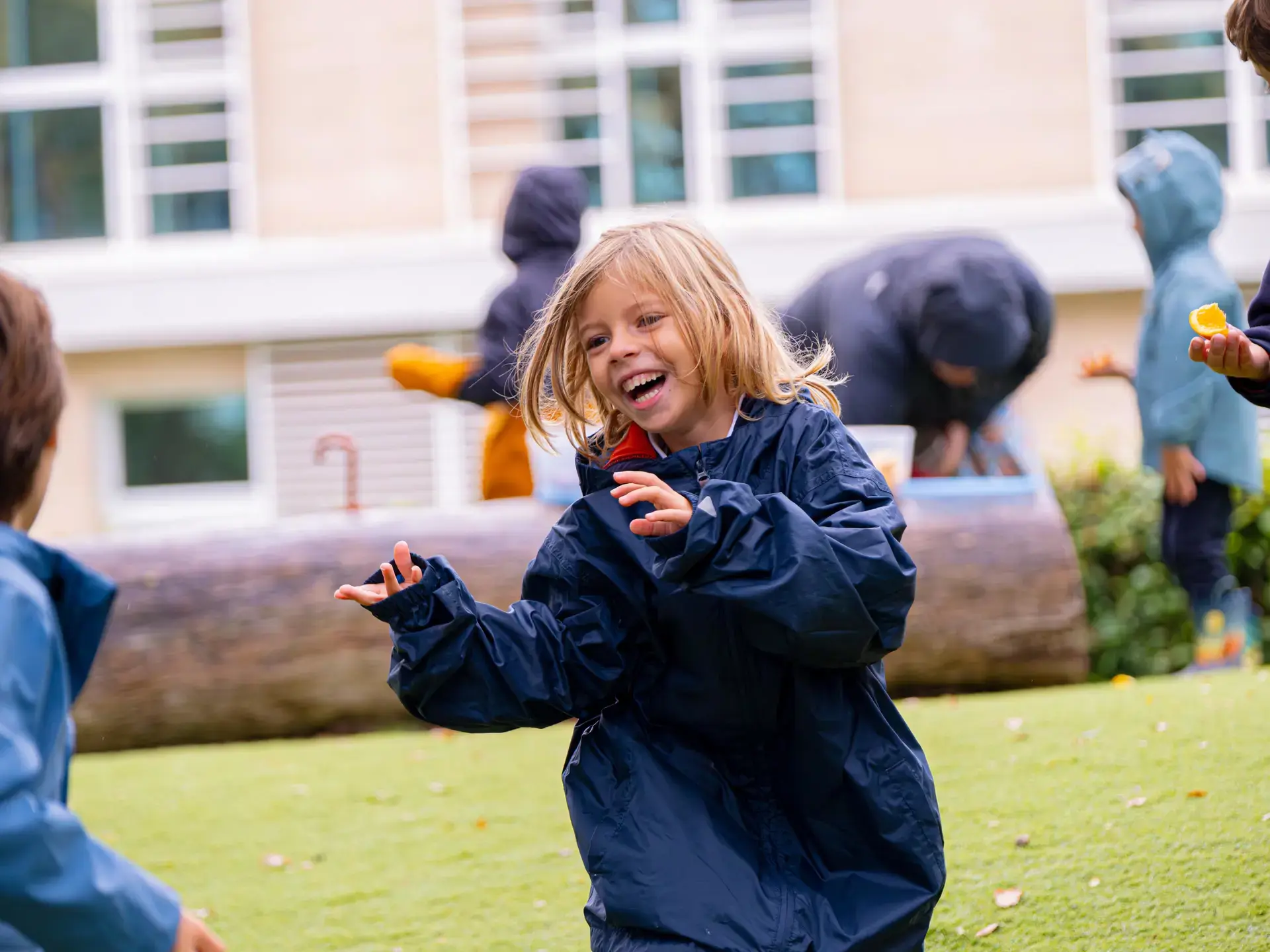 young student laughing and playing outdoors in a rain jacket during recess