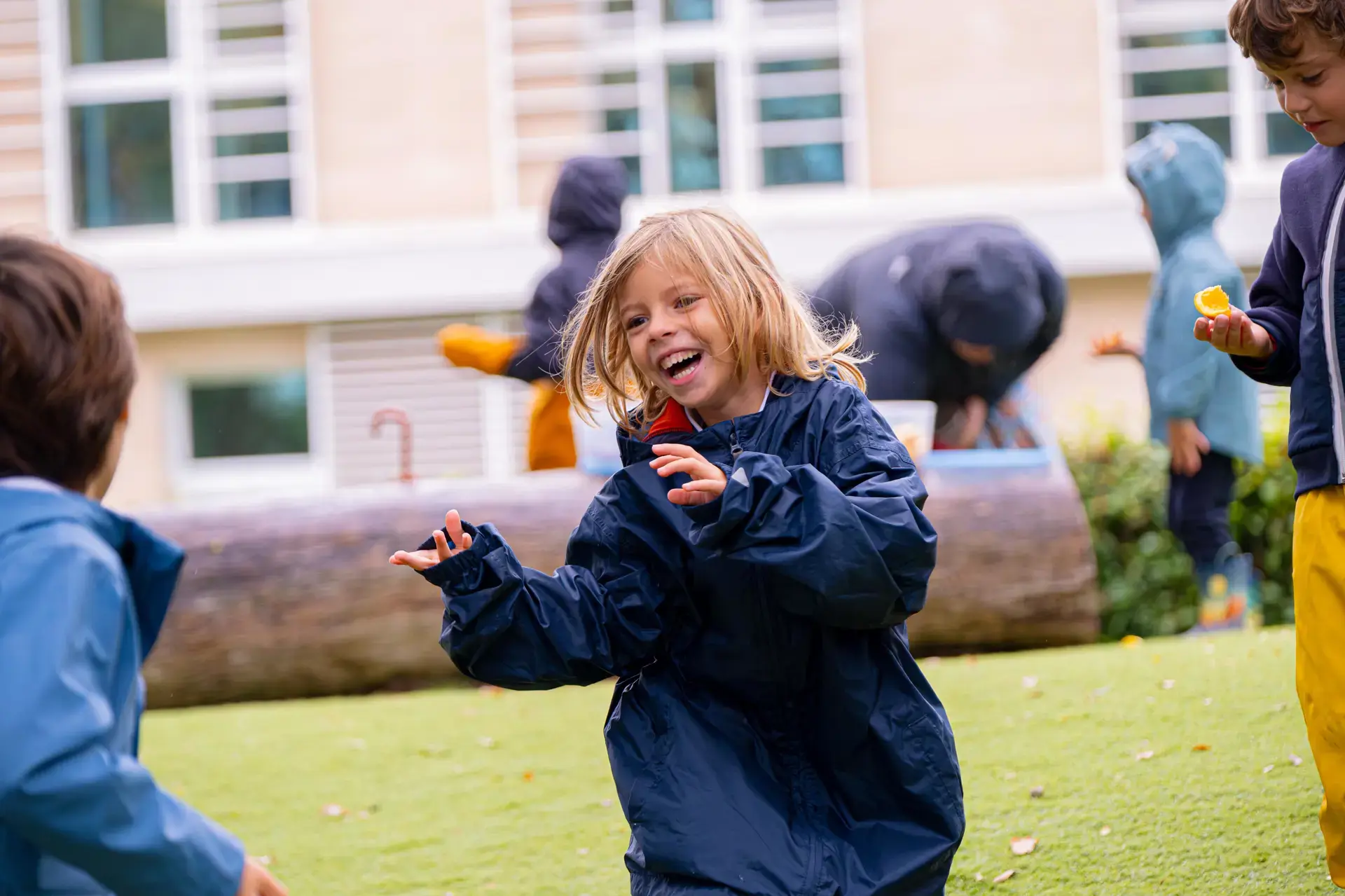 young student laughing and playing outdoors in a rain jacket during recess