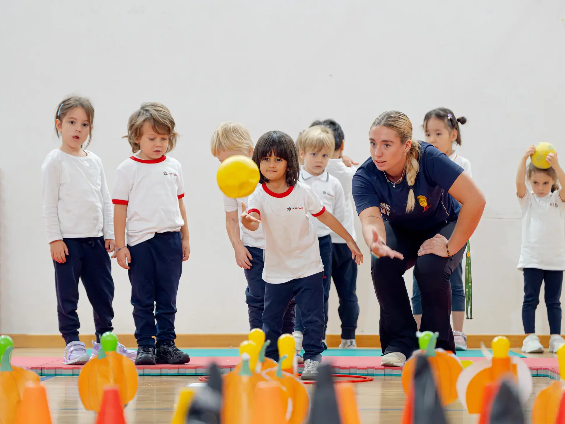 young students playing a ball toss game with their pe teacher in the gym