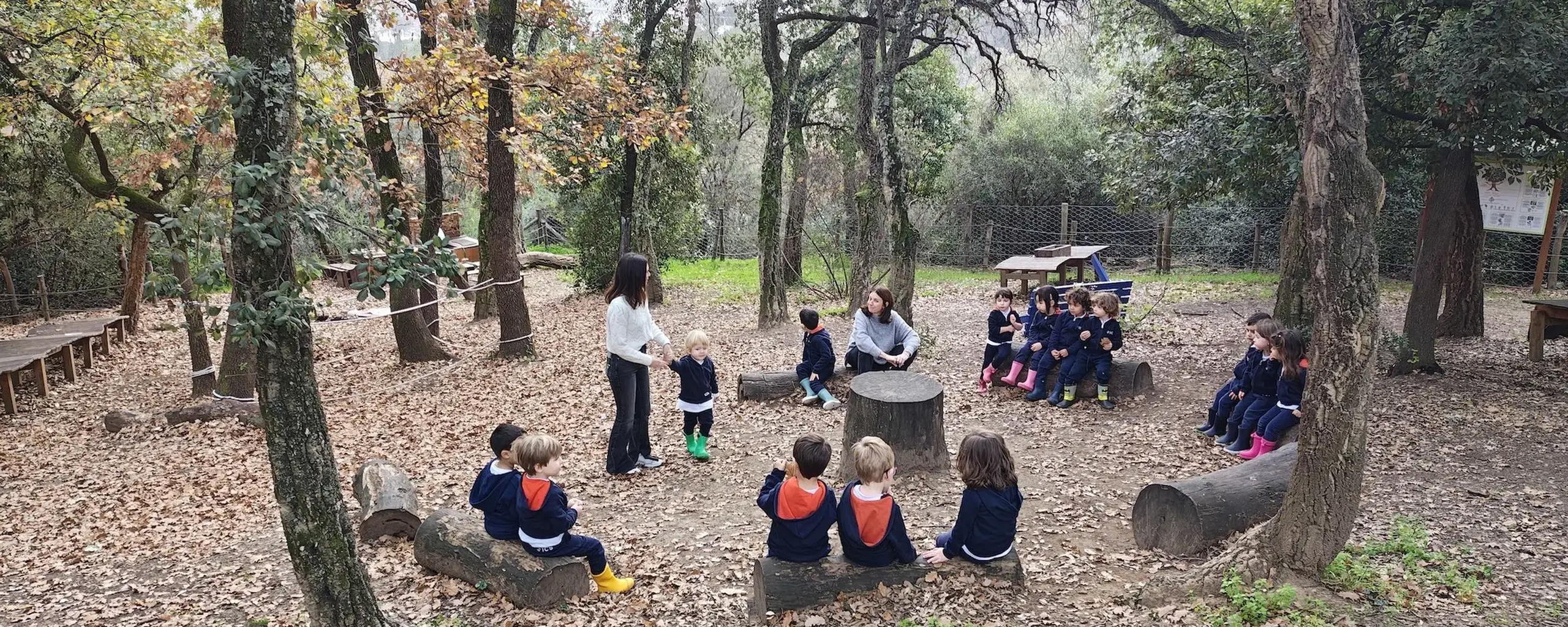 Rome International School students learning outdoors in a woodland setting with their teachers.