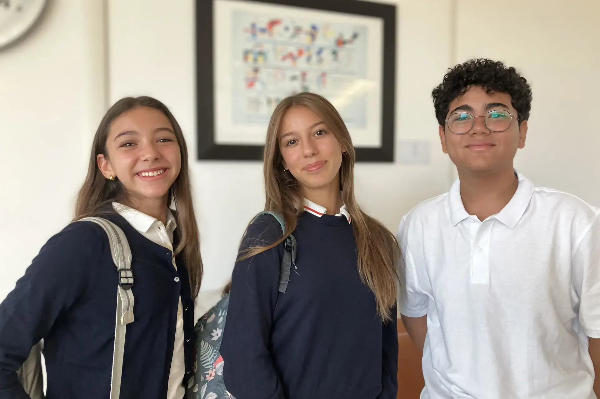 three students in uniform smiling together indoors.