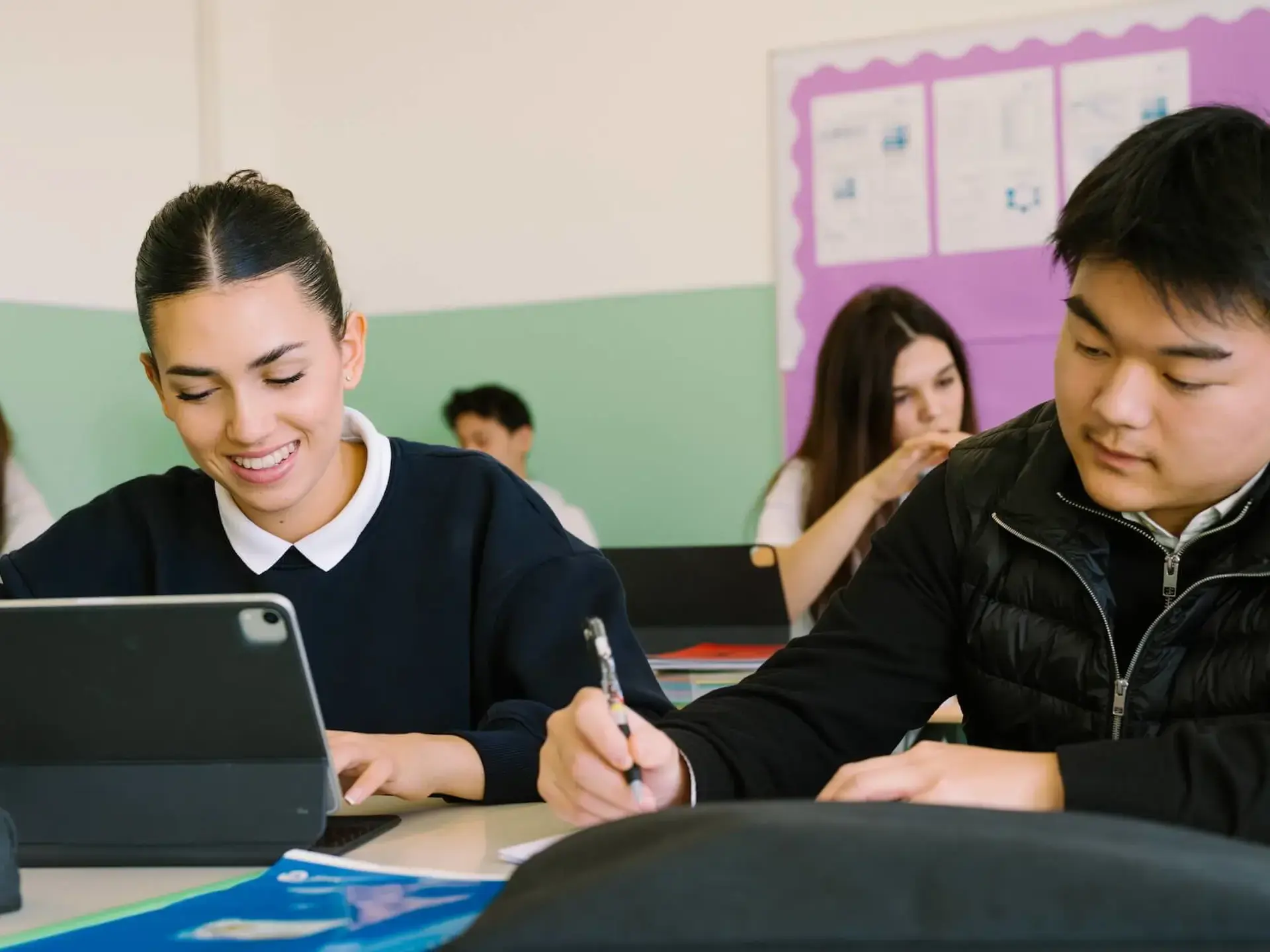 high school students working on a tablet and taking notes during class