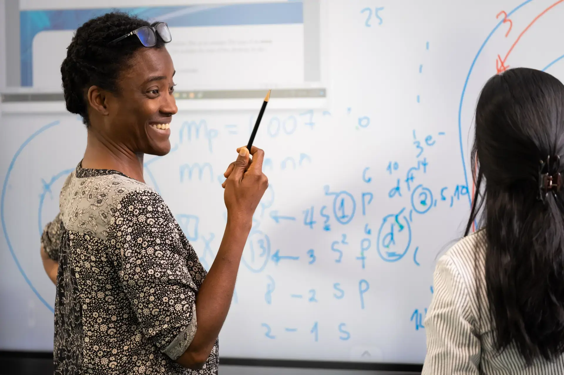 teacher pointing to equations on a whiteboard while explaining to a student