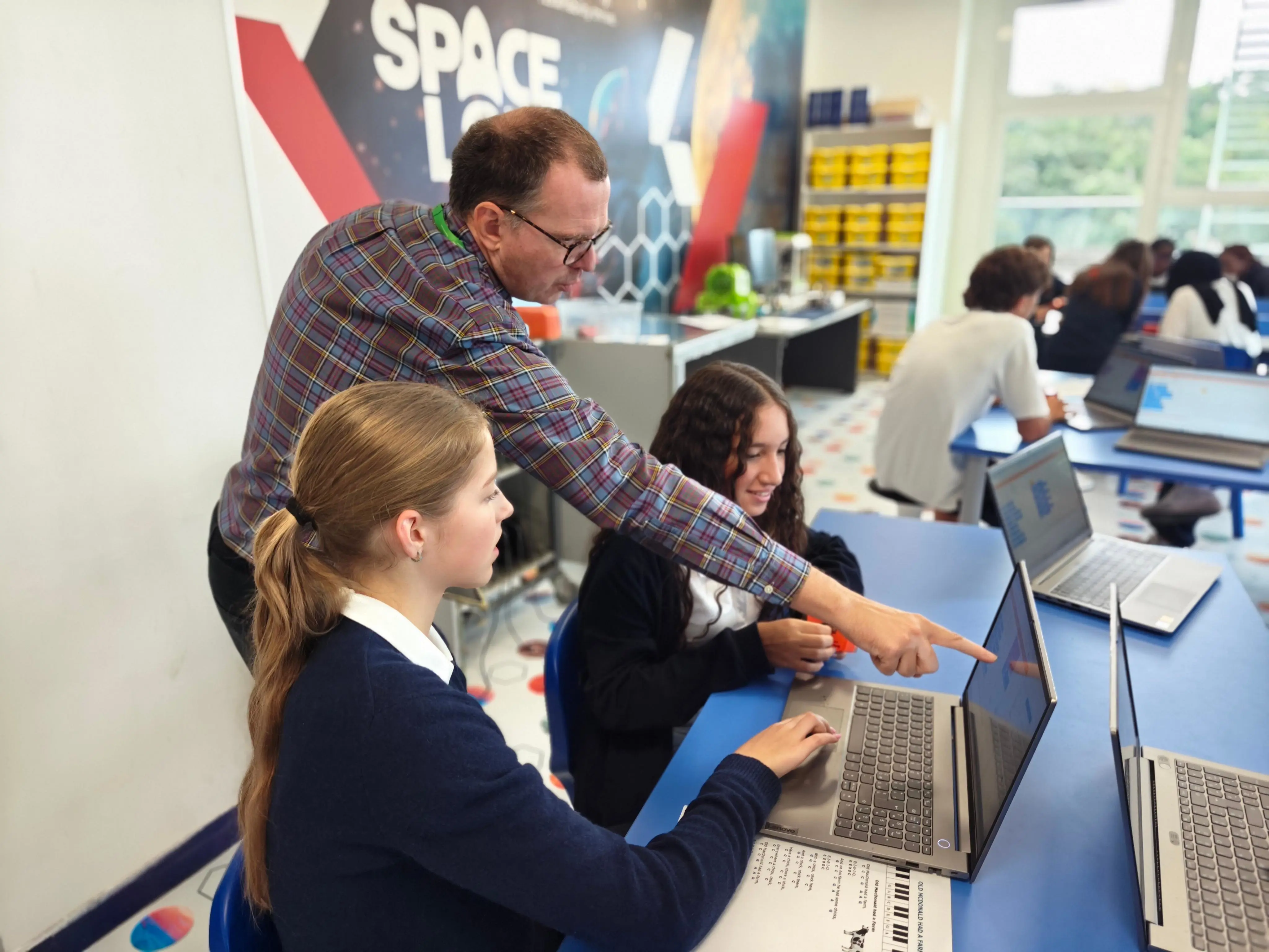 teacher helping students at their laptops in the Space Lab classroom.
