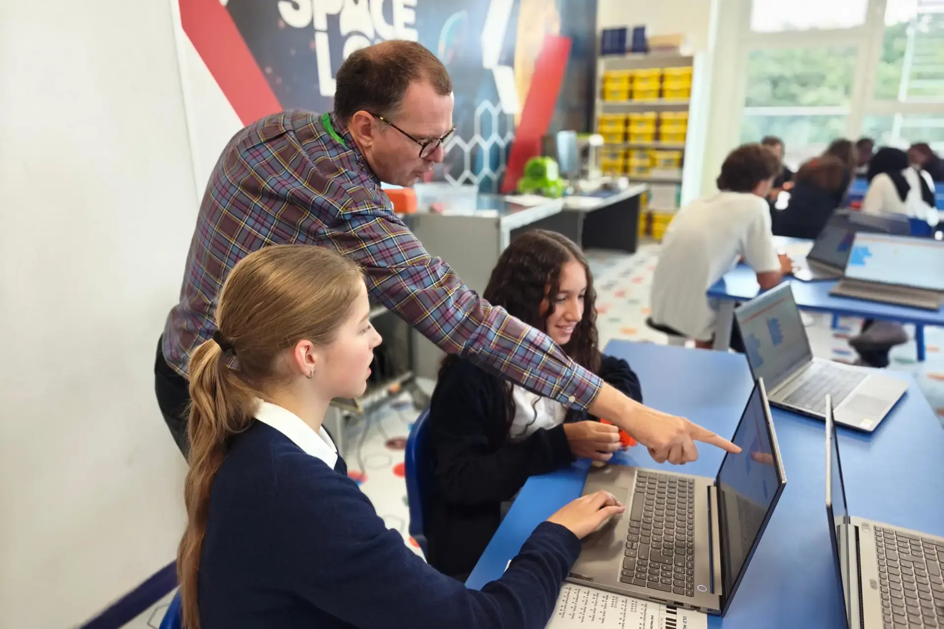 teacher helping students with a laptop assignment in a classroom