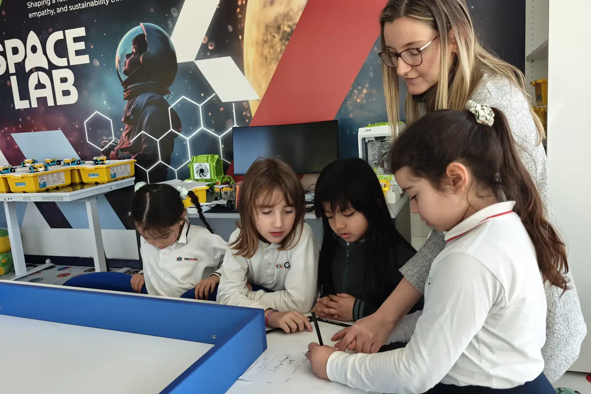 teacher guiding young students through an activity at their table in the Space Lab classroom.