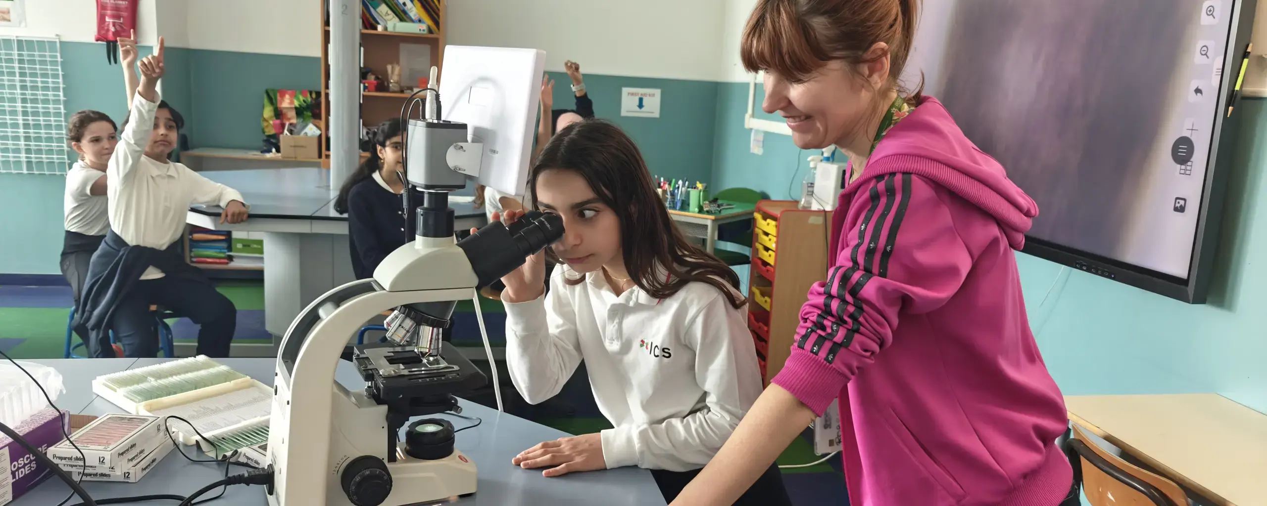 student looking through a microscope while her teacher assists in the science classroom.