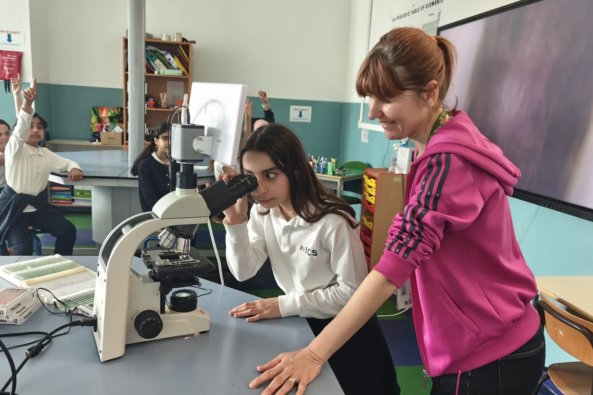 student looking through a microscope while her teacher assists in the science lab.