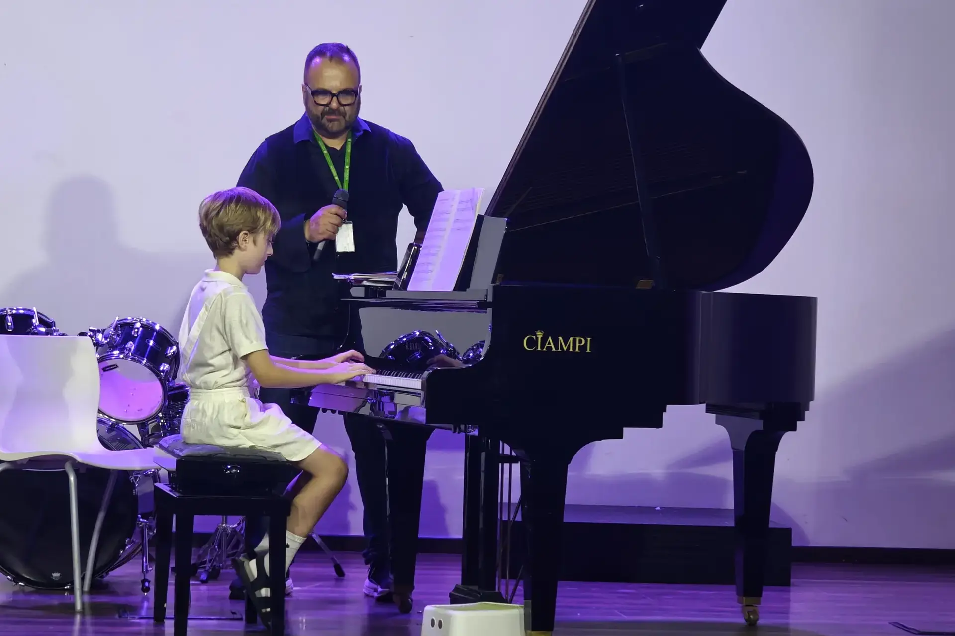 student playing grand piano on stage under purple lighting.