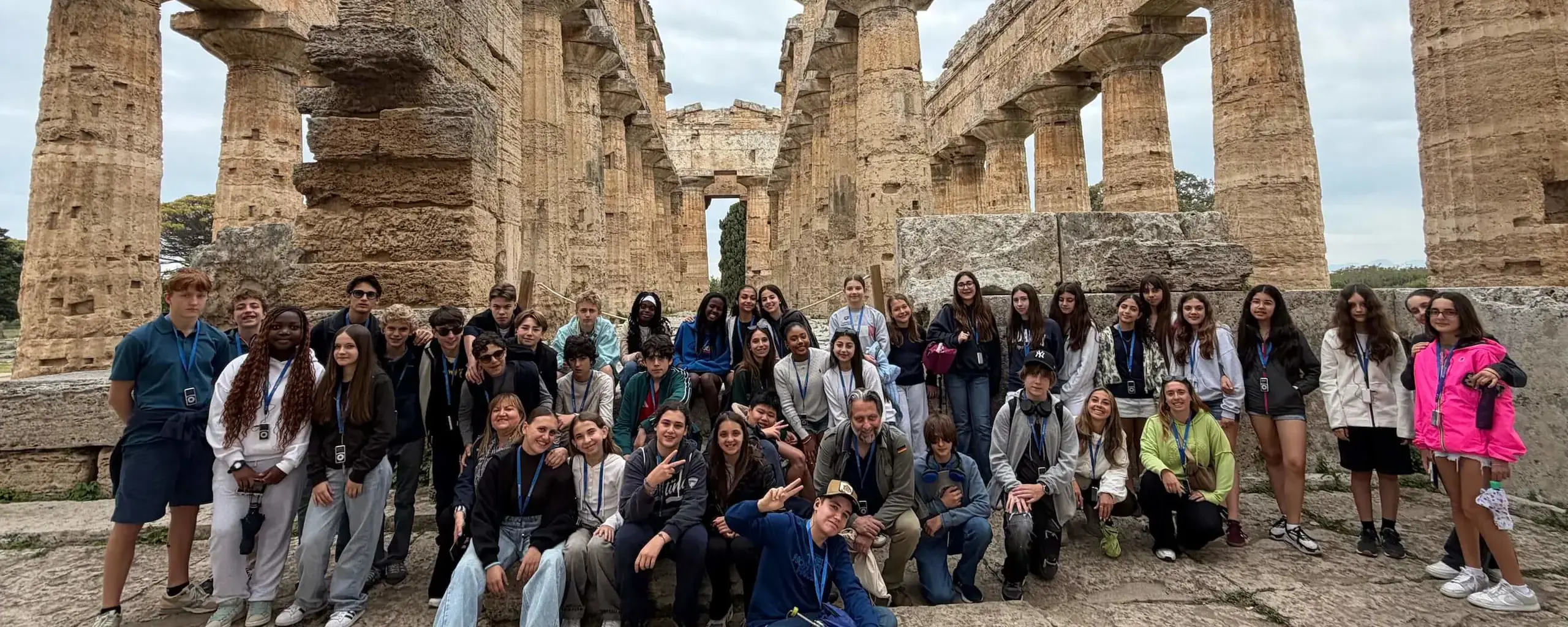 students and chaperones posing for a group photo in front of ancient greek temple columns during a school trip to italy