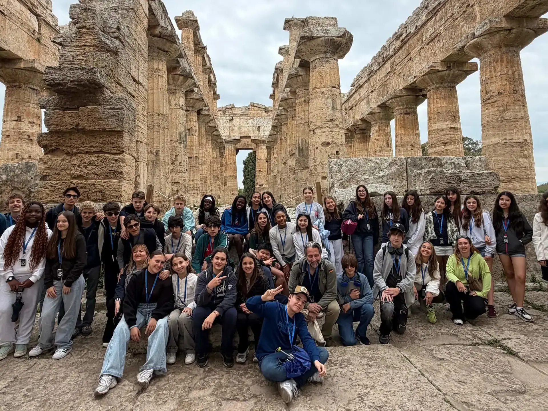 students and chaperones posing for a group photo in front of ancient greek temple columns during a school trip to italy