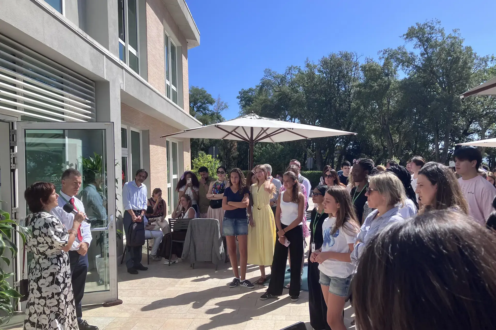 parents and students gathered outdoors listening to a speaker at a school assembly